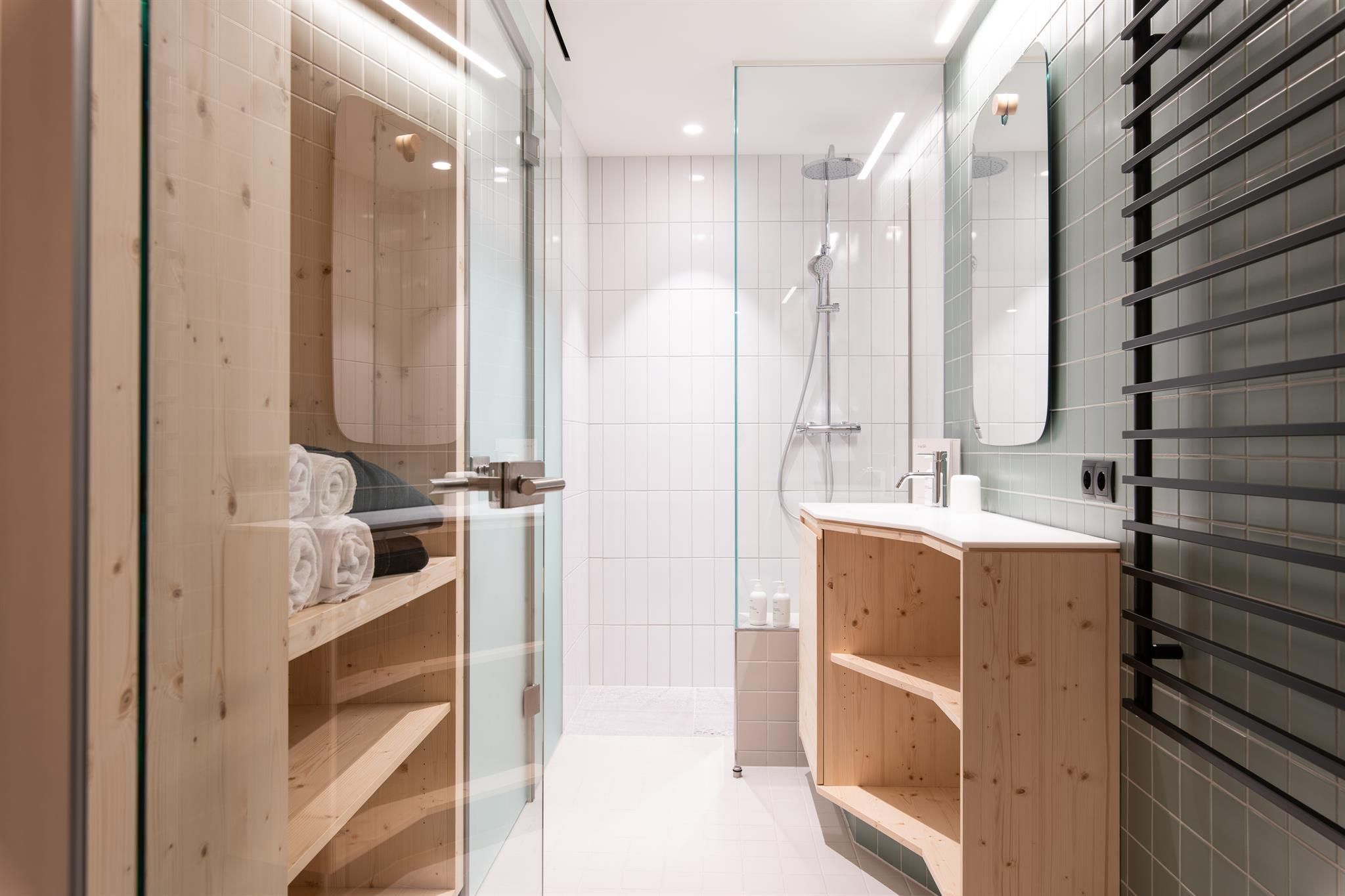 A modern bathroom with a glass shower and wooden shelves. The walls are brightly tiled and an elegant sink unit is present.
